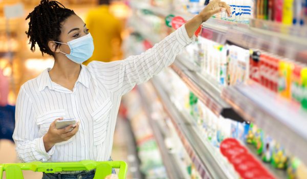 Grocery Shopping. African American Woman Wearing Protective Face Mask In Supermarket, Buying Food Products In Groceries Store Indoor. Female Buyer With Shop Cart In Hypermarket